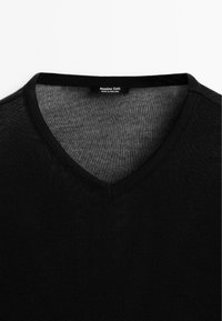 Czarny sweter z dekoltem w serek wykonany z teksturowanej dzianiny. Charakteryzuje się prostym wzornictwem, bez wzorów, z metką "Massimo Dutti, wyprodukowano w Portugalii".