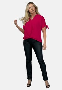 Fuksjowa bluzka z krótkim rękawem i dekoltem w serek, z węzłem w talii, w połączeniu z czarnymi dopasowanymi spodniami i czarnymi sandałami na wysokim obcasie.