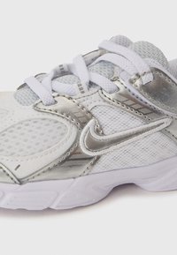 Hõbe- ja valge spordisaabas, millel on võrgupaneelid, pehmendusega tald ja valged nööbid koos metallilise Nike logoga küljel.