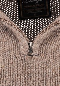 Beiger gestrickter Pullover mit hohem Kragen, ausgestattet mit einem silbernen Reißverschluss an der Vorderseite und einem strukturierten, weichen Stoff mit lockerem Gewebemuster.
