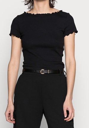 Camiseta negra acanalada con escote y bordes de las mangas en forma de ondas, combinada con pantalones de talle alto y un cinturón negro delgado con hebilla dorada.