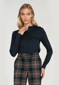 Czarna koszula henley z długim rękawem, charakteryzująca się zapięciem na guziki i miękką teksturą, zestawiona z wysokimi spodniami w kratę w ciemnozielonym i pomarańczowym kolorze.