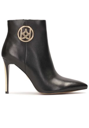 Schwarze Leder-Stiefelette mit spitzem Zeh, hohem Stiletto-Absatz und einem goldenen runden Logoakzent an der Seite. Glatte Textur und elegantes Design.
