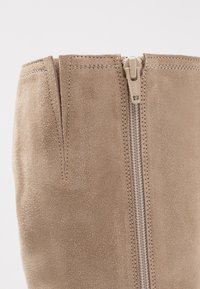 Bottine en daim beige clair, dotée d'une fermeture éclair centrale et d'accents cousus. Texture douce avec un design élégant et effilé.