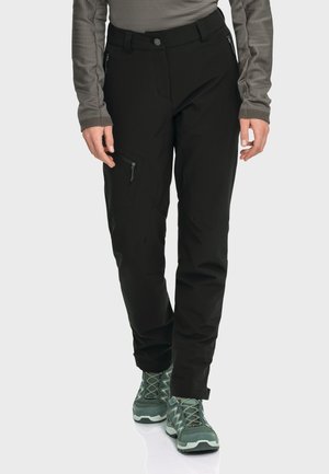 Schwarze wasserdichte Hosen mit schlankem Schnitt, mit Reißverschlusstaschen und verstellbarem Bund, kombiniert mit grünen Wanderschuhen mit strukturierten Sohlen.