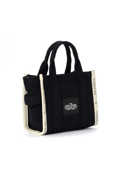 Saco tote preto da Marc Jacobs com borda branca, duas alças, bolso lateral e etiqueta de texto no centro da frente.