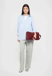 Lyseblå skjorte med knapper, grå vidde sweatpants og en bordeaux ruskinds crossbody taske. Sorte og hvide sko fuldender outfittet.