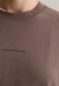 Felpa marrone con colletto rotondo a costine. Presenta il logo in rilievo nero "Marc O'Polo DENIM" sul davanti. Dettagli delle cuciture visibili.