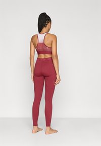 Leggings desportivos cor de vinho com uma cintura alta e soutien desportivo correspondente, apresentando uma parte traseira em rede e detalhes subtis de marca. Material liso e elástico.