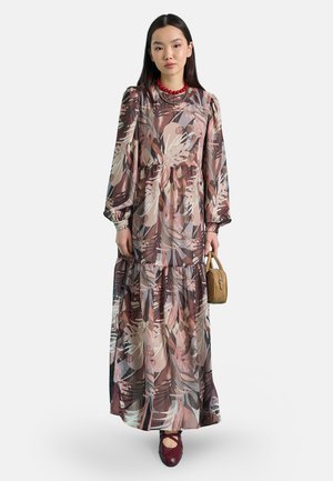 Donna con un lungo vestito floreale con maniche a sbuffo, collana rossa, che tiene una piccola borsa marrone e scarpe bordeaux con cinturini.