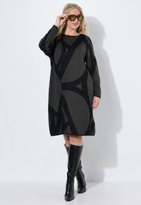 Abito di maglia con un motivo geometrico nero e grigio, maniche lunghe e vestibilità comoda, abbinato a stivali neri al ginocchio.