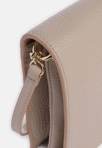 Borsa a mano in pelle beige con finitura testurizzata, accessori in metallo dorato e tracolla removibile. La vista laterale evidenzia le cuciture e i dettagli della fodera interna.