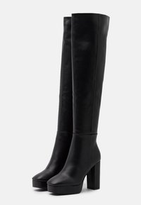 Par de botas altas de cuero negro con plataformas, tacones gruesos y de gran altura, de longitud hasta la rodilla y acabado suave.