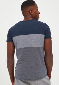 Short-sleeve t-shirt featuring navy top, grey middle panel, and striped bottom. Made of soft fabric with rounded hem and crew neck.