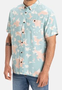Krátký rukáv košile na knoflíky v světle modré barvě s abstraktními růžovými a bílými vzory, s jednou kapsou na hrudi a tmavě hnědými knoflíky.