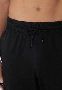 Pantalones de chándal negros con cintura elástica y cordón ajustable. Tejido suave y ligero con un corte holgado.