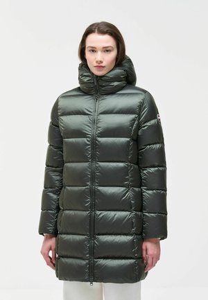 Frau trägt eine lange, dunkelgrüne Steppjacke mit hohem, gepolstertem Kragen und Frontreißverschluss, steht vor einem schlichten hellen Hintergrund.