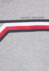 Szara bawełniana koszulka z wyrazistym wzorem graficznym w czerwone i białe oraz granatowe paski, z napisem "TOMMY HILFIGER" nadrukowanym powyżej.