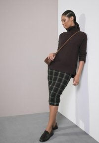 Pulover marron cu guler înalt, asortat cu o fustă tip creion în carouri alb-negru și verde, accesorizat cu o geantă bej tip crossbody și mocasini negri.