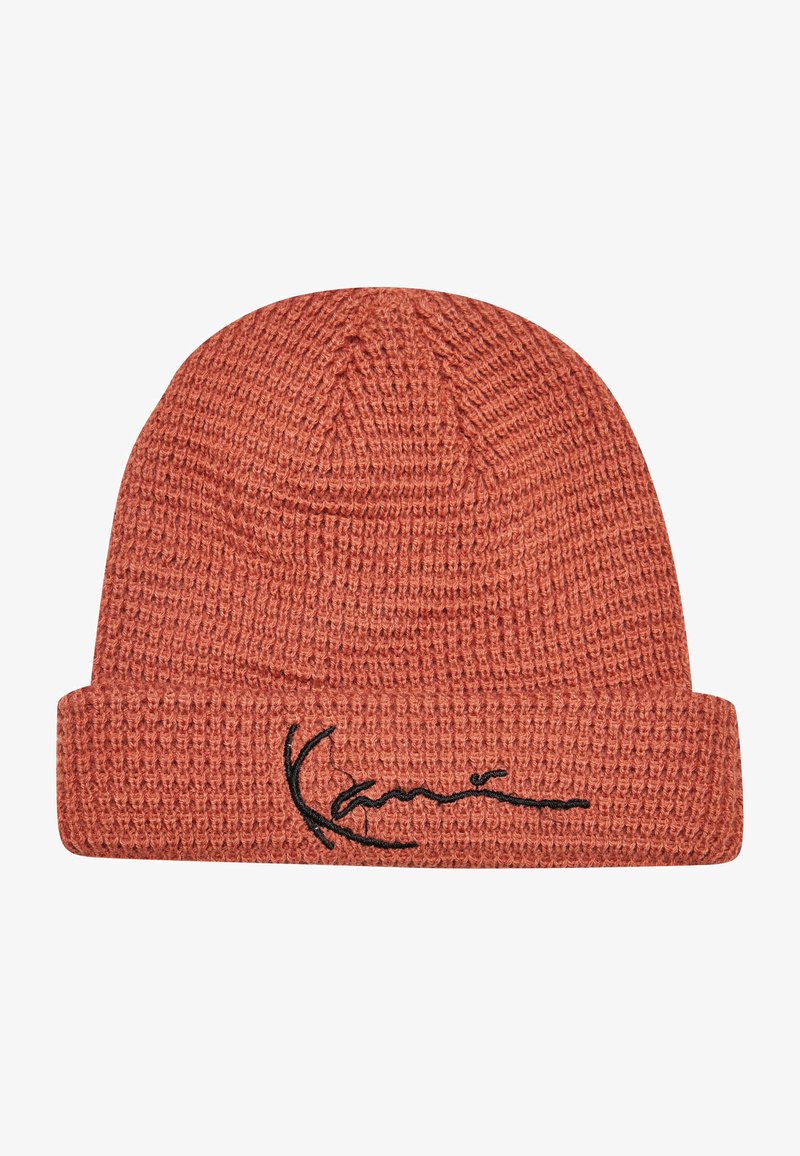 Gebreide beanie in een roestoranje kleur met een omgeslagen boord, voorzien van een zwart geborduurd logoontwerp aan de voorkant. Zachte textuur zichtbaar.