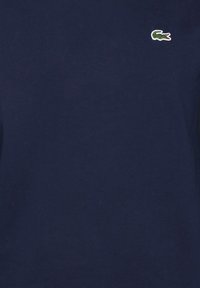 Tissu bleu marine foncé avec un petit logo de crocodile vert brodé près du côté supérieur droit.