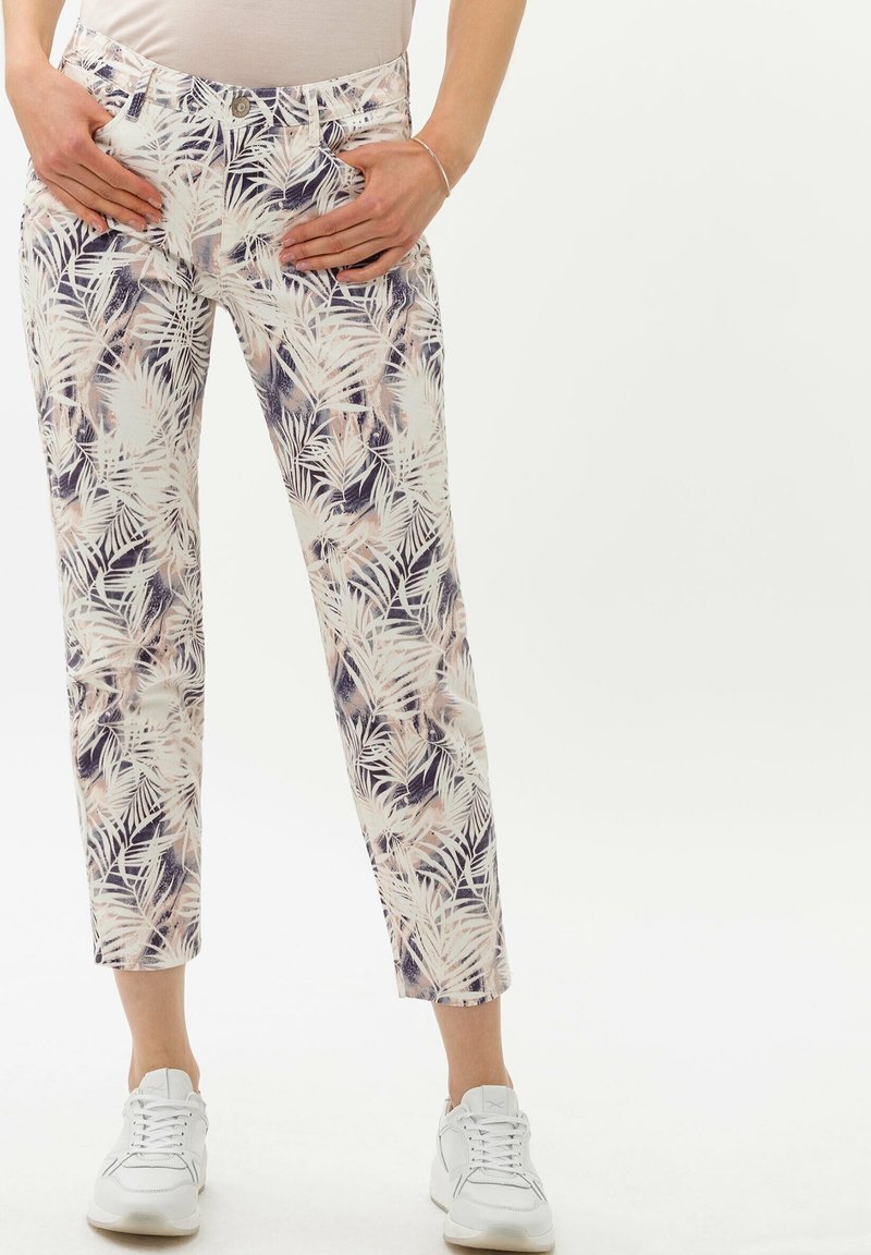 Pantalons blancs avec un motif de feuilles de palmier multicolore, présentant une coupe ajustée et une longueur sous le cheville. Associés à des baskets blanches.
