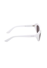 Lunettes de soleil blanches en forme d'œil de chat avec des verres gris et le logo "Guess" sur la branche, vues de côté sur un fond blanc.