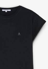 Schwarzes Baumwoll-T-Shirt mit rundem Halsausschnitt und umgeschlagenen kurzen Ärmeln. Verfügt über ein kleines gesticktes Totenkopf- und gekreuztes Schwert-Logo auf der Brust.