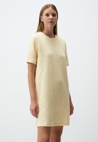 Korte mouwen jurk in een zachte, getextureerde lichtgele stof, met een losse pasvorm en een ronde halslijn. Eenvoudig, minimalistisch ontwerp.