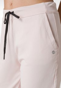 Ljusrosa sweatpants i mjukt material, med en svart dragsko i midjan, sidofickor och en liten logotyp på låret.