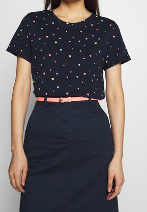 Laivastonsininen t-paita, jossa on värikkäitä sydänkuvioita, pyöreä kaula-aukko, lyhyet hihat, yhdistettynä ohueen vaaleanpunaiseen vyöhön ja tummaan hameeseen.