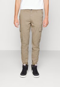 Beiga cargobyxor gjorda av bomull, med flera sidofickor, tapered bendesign och bärs med svarta högsneakers.