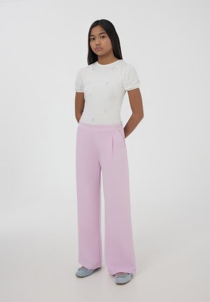 Top a maniche a sbuffo con piccole aperture, abbinato a pantaloni a gamba larga rosa pallido con vita alta. Completato con scarpe basse blu.