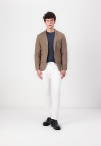 Brun linblazer över en marinblå t-shirt, tillsammans med vita jeans och svarta ankelstövlar. Blazern har två framfickor och en enkel knapp.