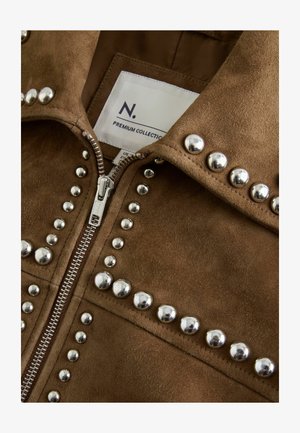 Braune Wildlederjacke mit einem zentralen Reißverschluss und silbernen Nietenakzenten entlang der Nähte. Das Etikett weist darauf hin, dass sie aus einer Premium-Kollektion stammt.