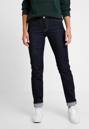 Dark blue denim jeans with a slim fit, featuring traditional five-pocket design, contrast stitching, and cuffed hems. Paired with white sneakers.
