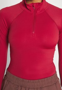 Rote Langarm-Zip-up-Oberteile aus glattem, dehnbarem Material; verfügt über einen Stehkragen und flache Nähte für zusätzlichen Komfort.