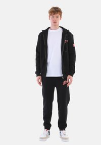 Black zip-up hoodie and black sweatpants set, with a white T-shirt underneath. Features logo accents. Sneakers with white, red, and gray detailing.