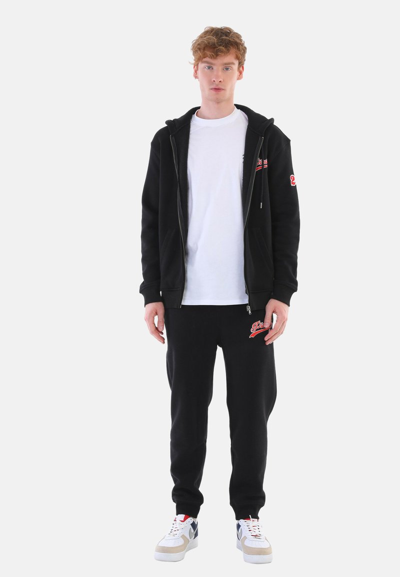 Black zip-up hoodie and black sweatpants set, with a white T-shirt underneath. Features logo accents. Sneakers with white, red, and gray detailing.