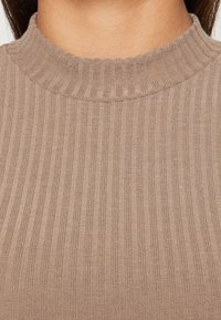 Tessuto a maglia rigata marrone con un colletto alto e textures. La superficie presenta strisce verticali, creando un aspetto strutturato.