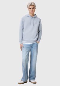 Felpa azzurra con cappuccio regolabile, polsini a coste e un piccolo logo. Abbinata a jeans azzurri a gamba dritta e sneaker bianche.