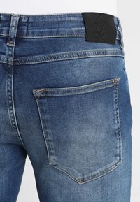 Blå denimjeans med en bakficka, lädermärke och en blekt textur med en avsmalnande design. Inga synliga sömnadsdetaljer.