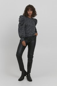Sort mønstret sweater med puffede ærmer, parret med tætsiddende sorte læderbukser og ankelstøvler. Glat tekstur, afslappet design.
