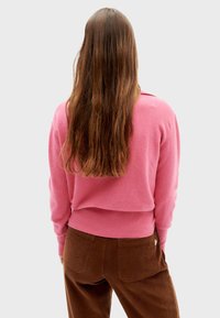 Roze cropped sweater met een ronde halslijn en lange mouwen, gecombineerd met bruine corduroy broek met achterzakken. Zachte stoftextuur.
