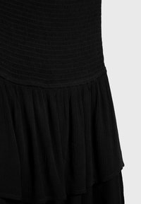 Robe noire avec un corsage texturé et smocké, et un ourlet à volants en couches. Le tissu est doux et léger, favorisant le mouvement et la fluidité.