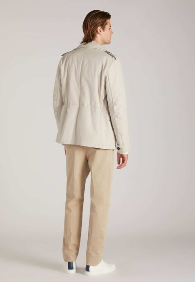 Lichtbeige jas met een ontspannen snit, schouderepauletten en een geraffineerde taille, gecombineerd met lichtbeige broeken en witte sneakers.