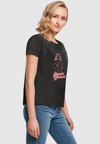 Sort bomulds T-shirt med rund halsudskæring. Har et pink grafik af en kvindelig figur og teksten "Wonder Woman" i kursiv. Korte ærmer.