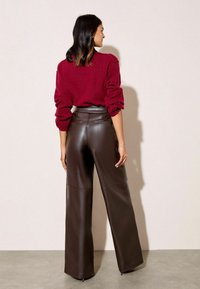 Brūnas ādas platas kājas bikses ar augstu vidukli un aizmugures kabatām, apvienotas ar sarkanu adītu džemperi ar apjomīgām piedurknēm.