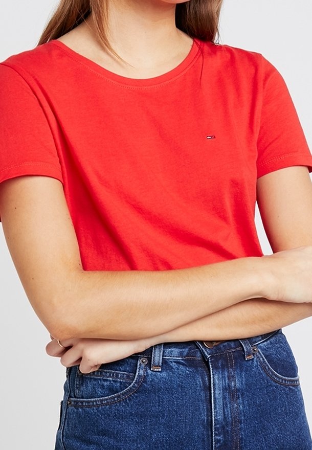 T-shirt en coton rouge à col rond, manches courtes, avec un petit logo sur la poitrine, associé à un jean en denim bleu taille haute.