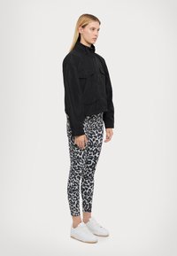 Veste noire courte avec deux poches avant, associée à un legging imprimé léopard noir et blanc et des baskets blanches. Tissu lisse, coupe décontractée.